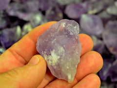 One raw purple amethyst stone 40mm on hand with background with some crystals