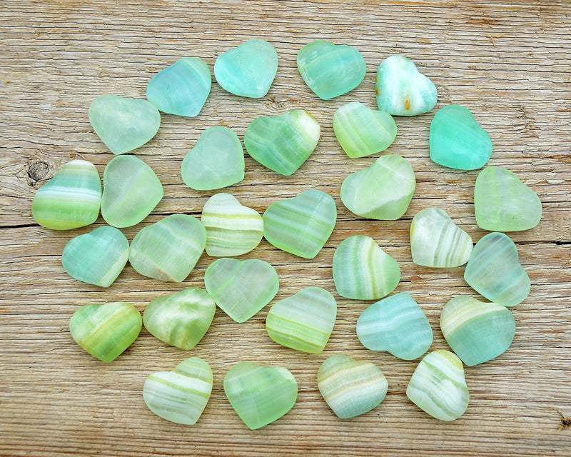 Several small green pistachio calcite crystal hearts 25mm-35mm on wood table