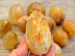 One golden healer quartz free form stone on hand with background with some crystals on wood table