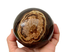 One chocolate calcite sphere 90mm on hand with white background