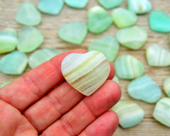 One mini green pistachio calcite crystal heart 25mm on hand with background with several hearts on wood table