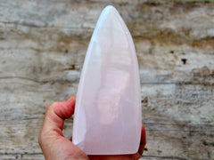 One large pink mangano calcite free form stone 115mm on hand with wood background