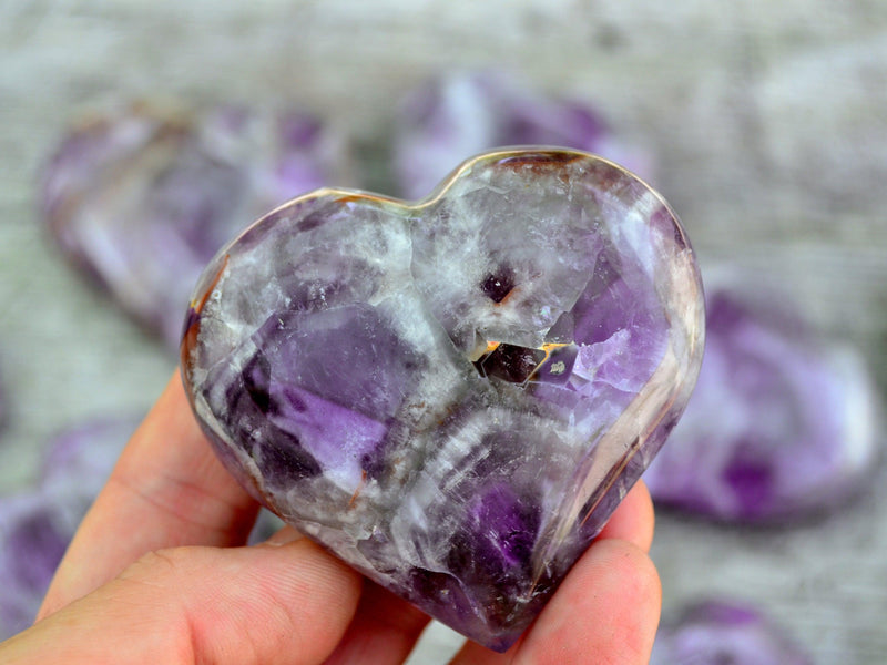 One chevron amethyst heart 70mm on hand with background with some hearts on wood table