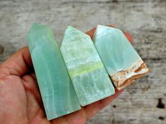 Three banded pistachio calcite obelisks 55mm-60mm on hand with wood background