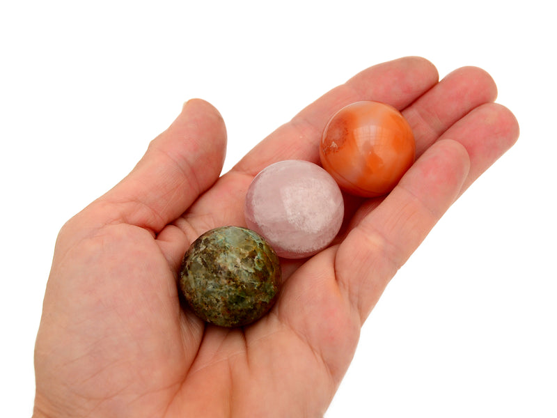 Orange carnelian, pink quartz and chrysocolla spheres 30mm on hand with white background