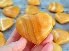 One orange calcite heart shapped stone 55mm on hand with background with some stones on wood table
