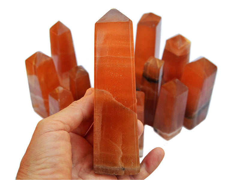 One large honey calcite crystal tower 140mm on hand with background with some obelisks on white