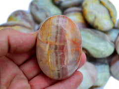 One pink banded onyx palm stone 50mm on hand with background with several crystals on white