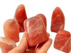 One small rose calcite crystal 40mm on hand with background with some specimens on white