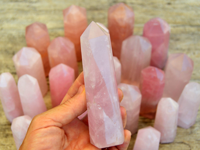 One rose quartz crystal obelisk on hand with background with some towers on wood table