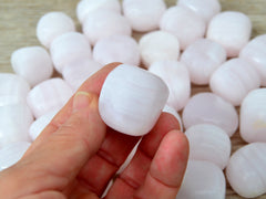 One mangano calcite mini tuble mineral 25mm on hand with some stones on wood table