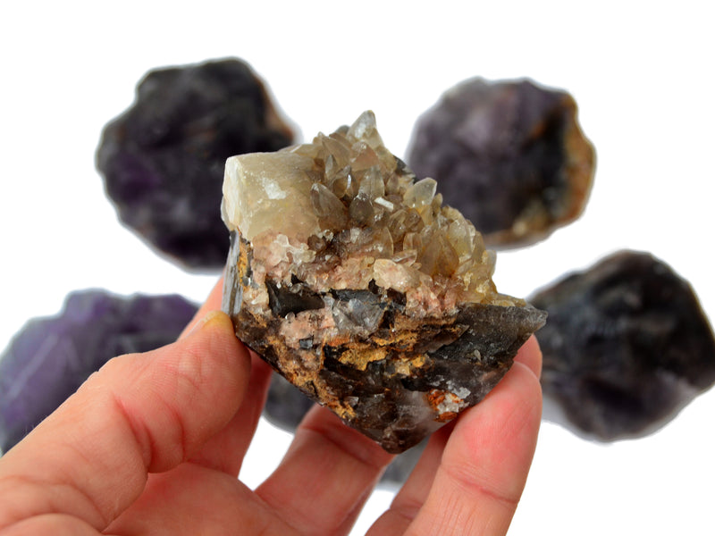 One raw purple fluorite with white quartz inclusions on hand with background with some minerals on white