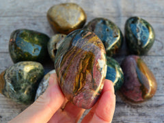One salmon and mustard yellow ocean jasper tumbled stone on hand with background with some minerals on wood table