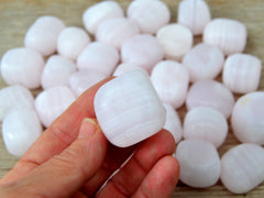 One pink mangano calcite tumbled crystal 20mm on hand with background with some stones on wood table