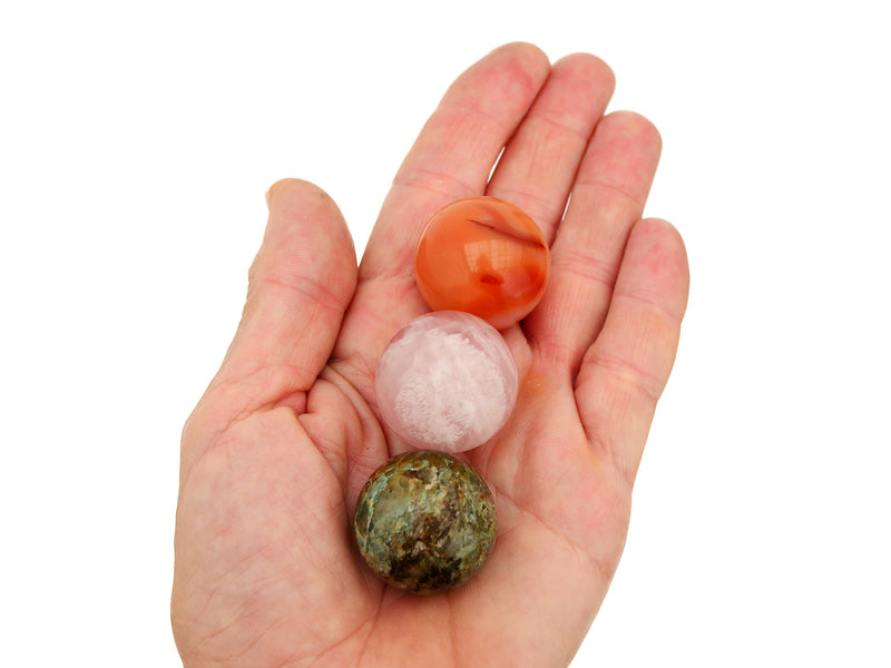 Green chrysocolla, orange carnelian and rose quartz spheres 30mm on hand with white background