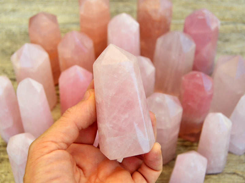 One pink quartz faceted point on hand with background with some towers on wood table