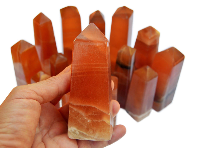 One natural honey calcite crystal obelisk 110mm on hand with background with several towers on white