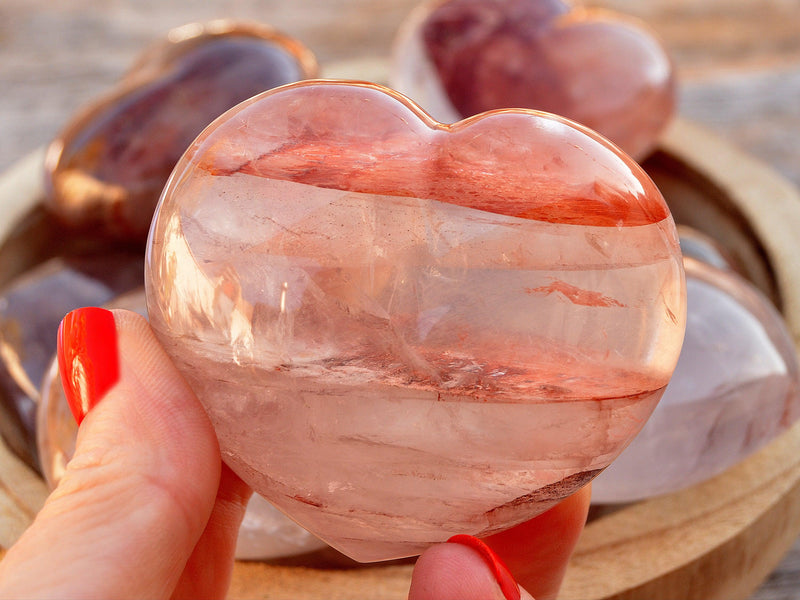 One large fire quartz heart stone 67mm on hand with background with some hearts inside a wood bowl