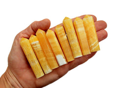 Eight small orange calcite faceted crystal points 50mm-60mm on hand with white background