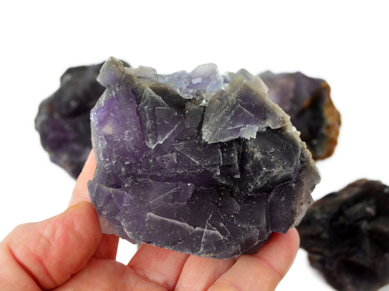 One raw cubic purple fluorite on hand with background with some minerals