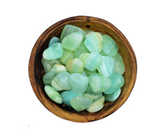 Several samll green calcite heart shapped crystals inside a wood bowl on white background