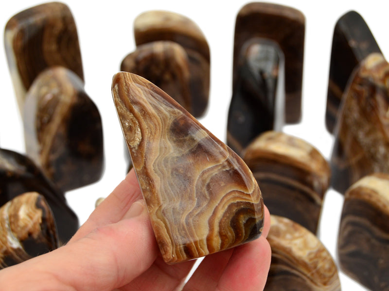 One chocolate calcite free form stones 65mm on hand with background with some stones on white