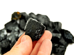 One raw tourmaline stone 25mm on hand with background with some crystals on white