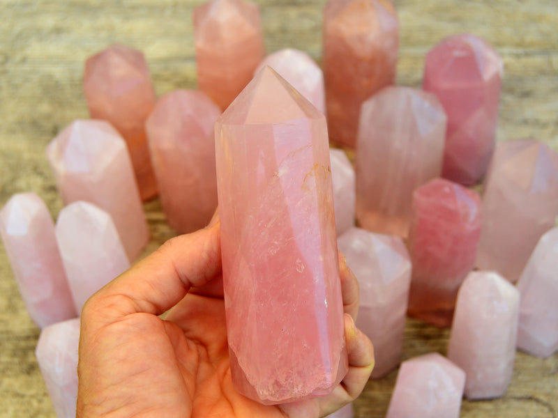 One large pink quartz faceted point on hand with background with some towers on wood table