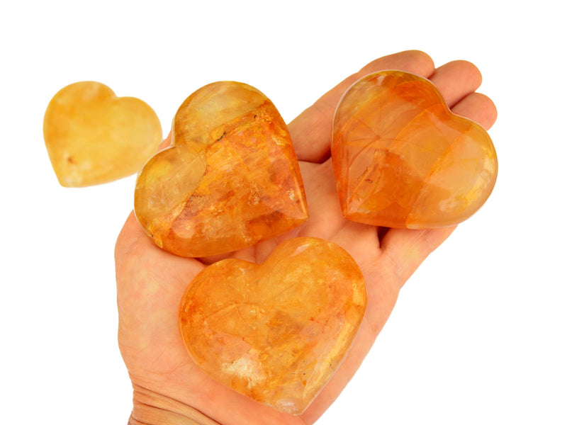 Three yellow hematoid quartz hearts on hand with white background