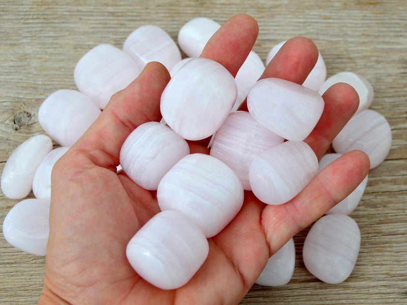 Pink mangano calcite tumbled crystals on hand with background with some stone on wood 