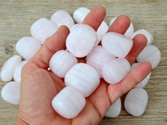 Pink mangano calcite tumbled crystals on hand with background with some stone on wood 