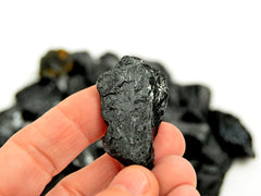 One raw tourmaline stone 40mm on hand with background with some crystals on white