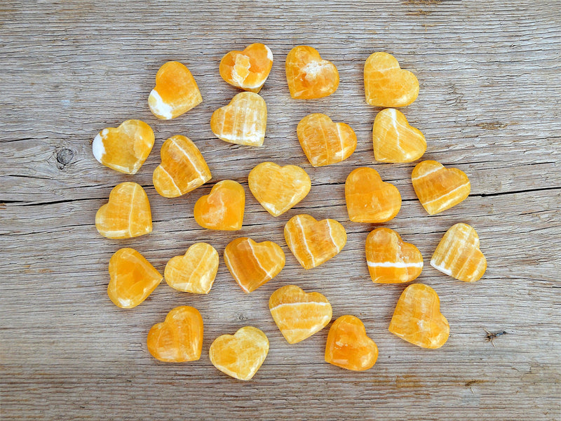 Several small orange calcite crystal hearts 30mm-35mm on wood table