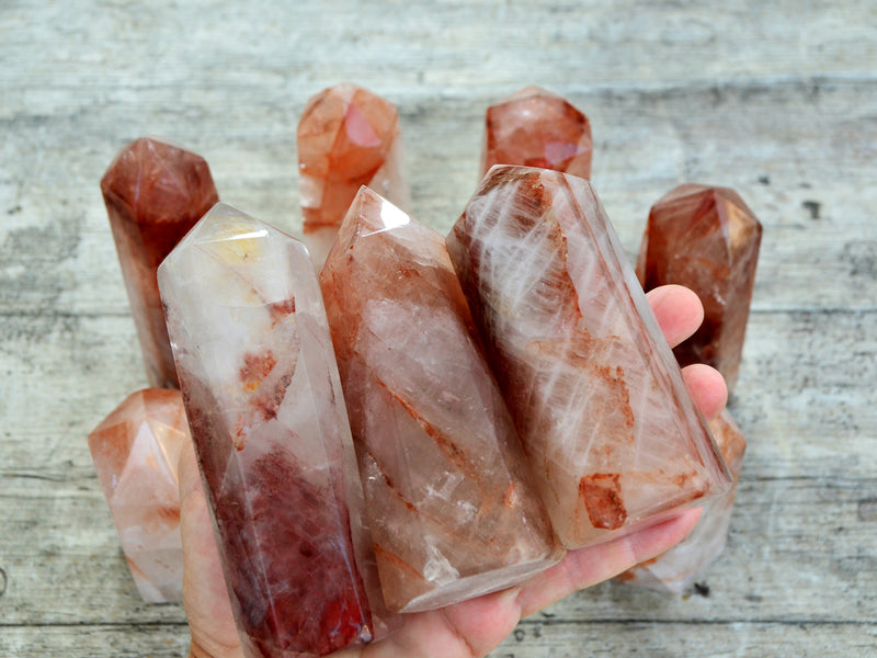 Three faceted fire quartz points on hand with background with some stones on wood table