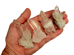 Four small clear quartz clusters 40mm-50mm on hand with white background