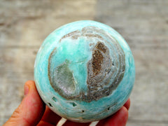 One large caribbean blue calcite sphere 80mm on hand with wood background