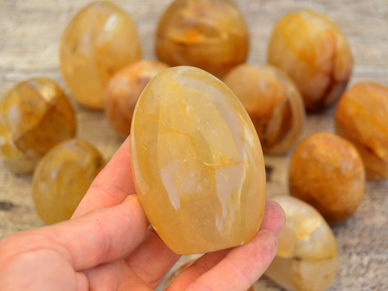 One golden healer quartz free form stone on hand with background with some crystals on wood table