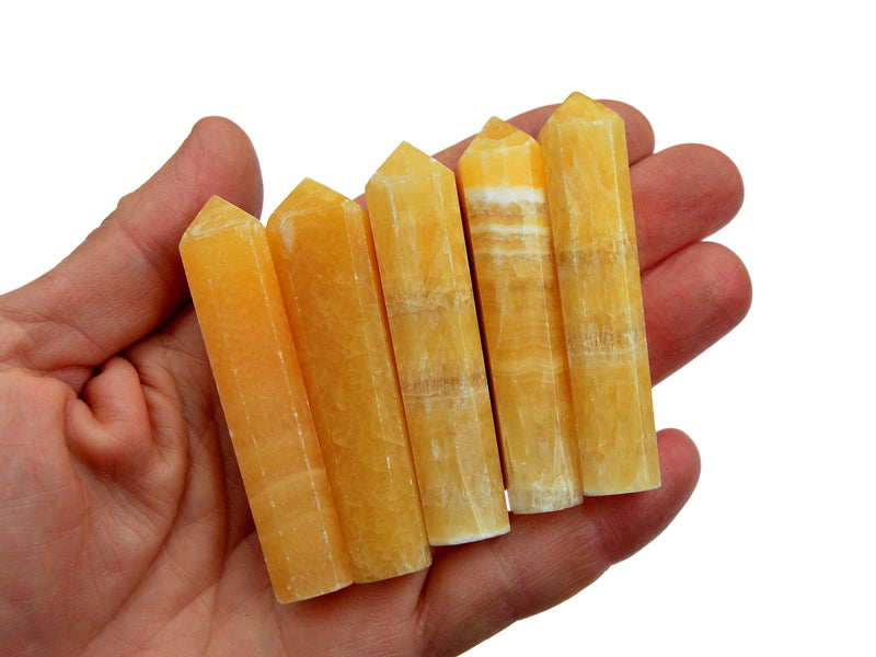 Four small orange calcite crystal tower 50mm-60mm on hand with white background