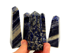 One lapis lazuli crystal obelisks 80mm on hand with background with some lapis stones
