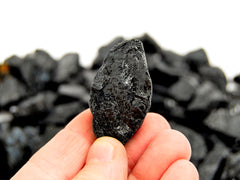 One raw tourmaline stone 50mm on hand with background with some crystals on white