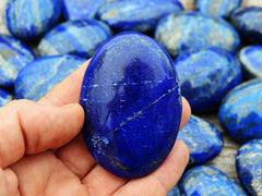One blue lapis lazuli palm stone crystal on hand with background with several stones on wood table