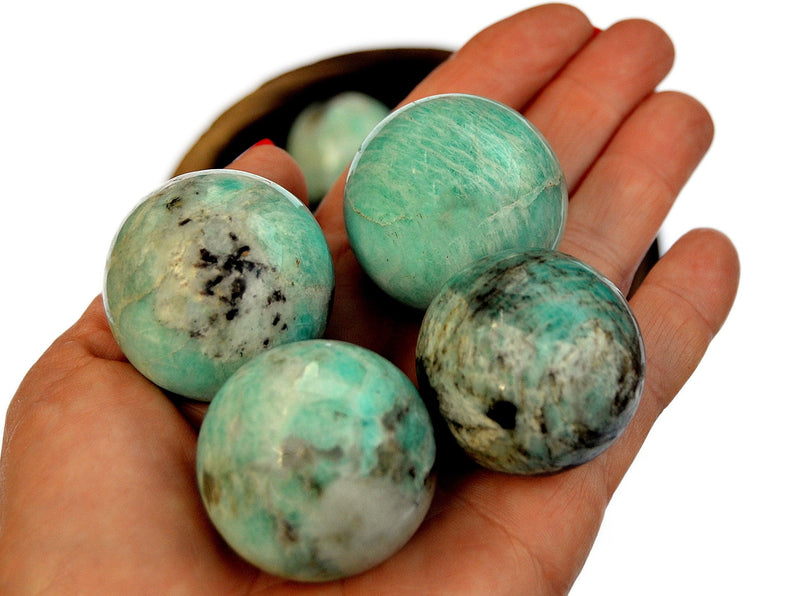 Some amazonite sphere stones 35mm-40mm on hand with background with some crystals inside a wood bowl