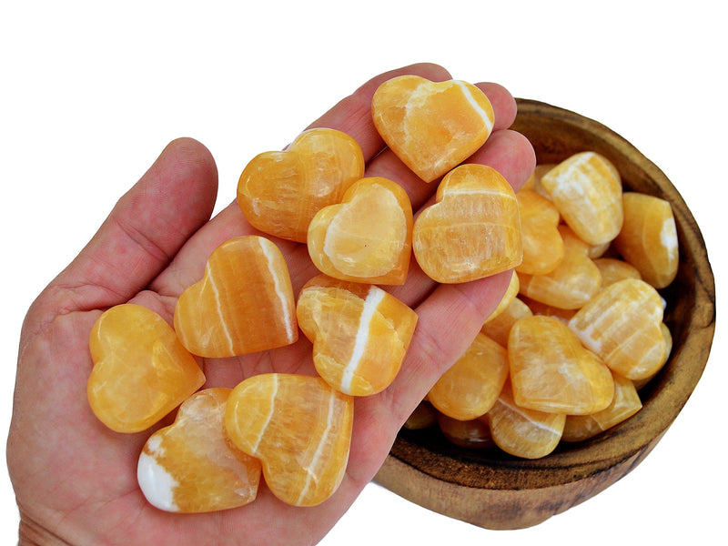 Ten orange calcite crystal hearts 30mm-35mm on hand with background with some hearts inside a wood bowl on white