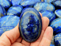 One lapis lazuli palm stone crystal on hand with background with several stones