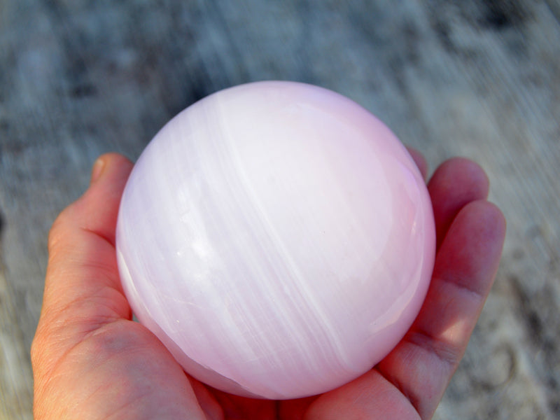 One large pink mangano calcite sphere 65mm on hand with wood background