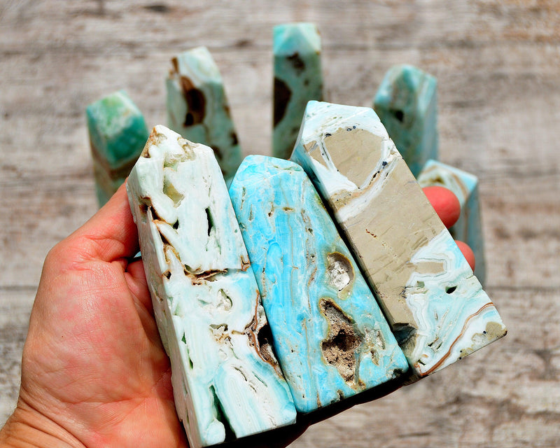 Three druzy blue aragonite crystal obelisk on hand with background with several crystals on wood table