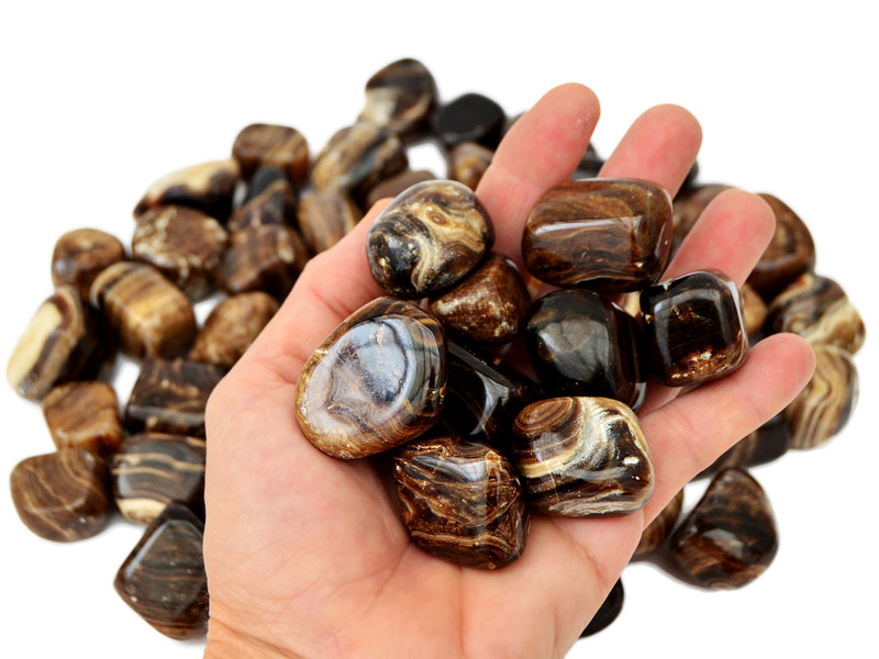 Some chocolate calcite tumbled on hand with background with several crystals on hand