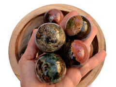 Four ocean jasper sphere minerals 45mm-55mm on hand with background with some crystals inside a wood bowl