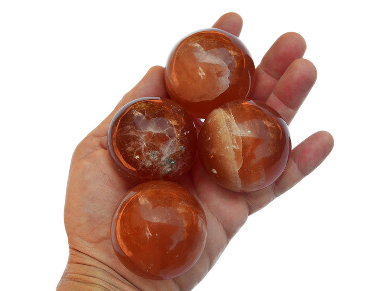 Four honey calcite crystal spheres 50mm on hand with white background