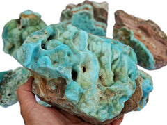 Large raw blue aragonite specimen on hand with background with some stones on white